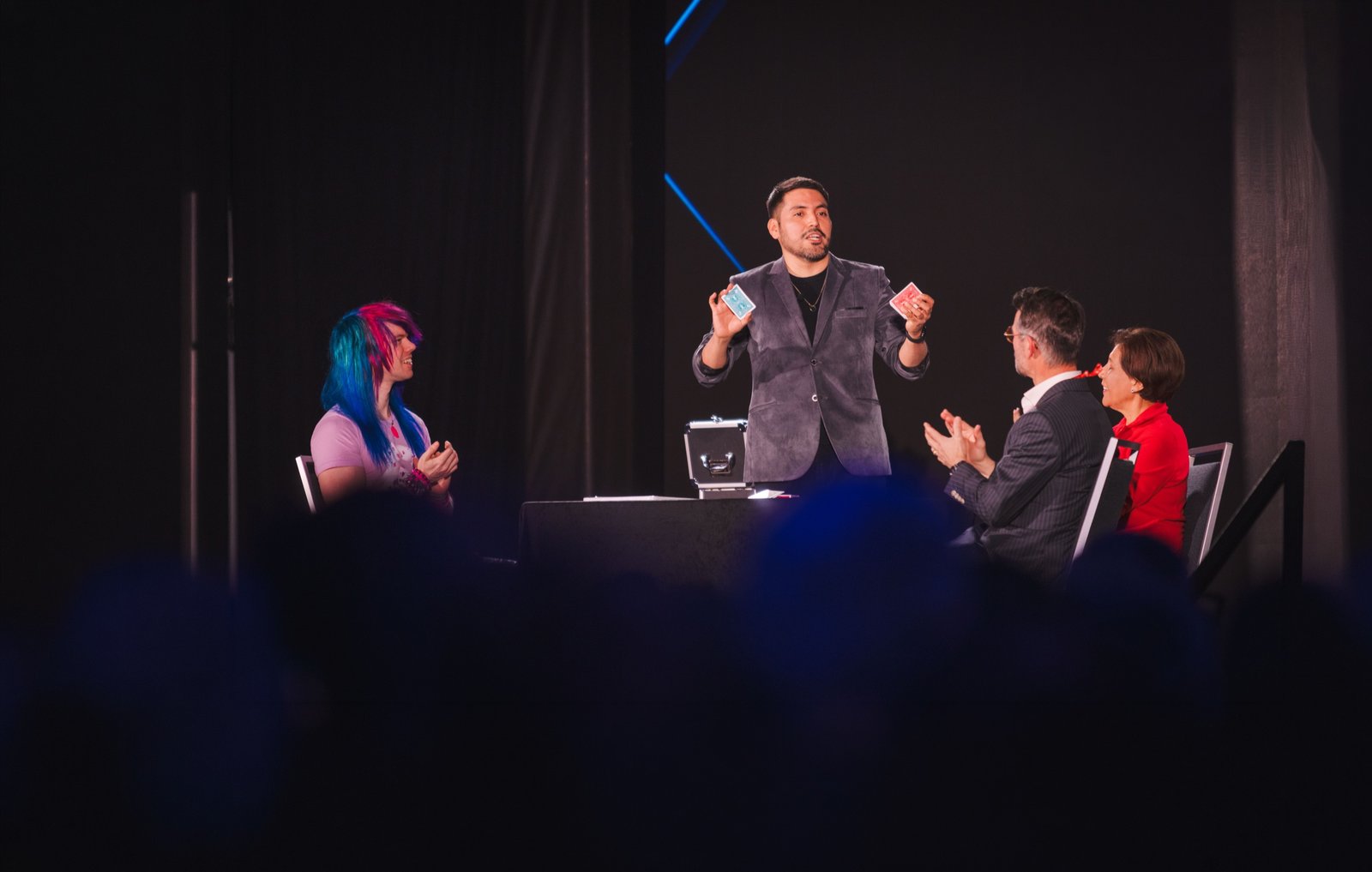 Alejandro performing card magic on stage with audience volunteers